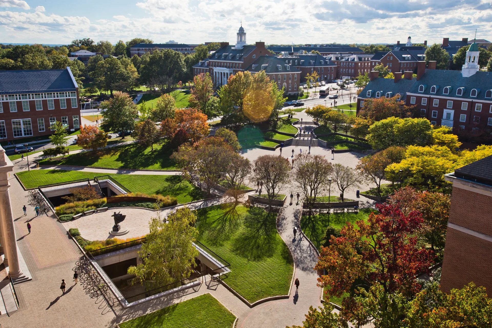 Aerial view of Hornbake Plaza at the University of Maryland, showing walkways, trees with fall foliage, and surrounding red-brick academic buildings under a partly cloudy sky.